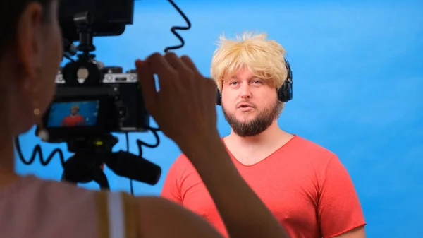 身穿粉色T恤、头戴假发的胖子在蓝色背景下写了一篇视频博客. — 图库照片