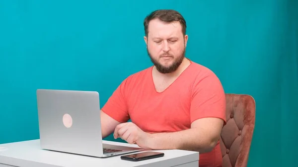 Il giovane uomo d'affari felice in una t-shirt rosa lavora su un computer portatile e parla con la macchina fotografica su uno schermo verde. Ritratto di un uomo parlante che guarda nel suo portatile. Uomo che lavora alla sua scrivania in ufficio. — Foto Stock