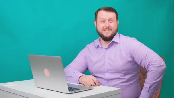 Junger glücklicher Geschäftsmann lächelt und spricht in die Kamera. Porträt eines lachenden Mannes beim Blick auf seinen Laptop. Mann am Schreibtisch im Büro — Stockvideo