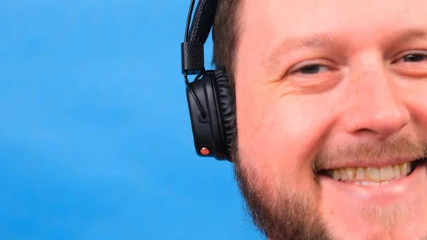 Bearded funny smiling cute fat man in a pink T-shirt listens to music and dances on a blue background, close-up, copy space.