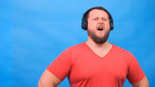 Joyeux homme gras charismatique dans des écouteurs isolé et rose t-shirt sur un fond bleu. écouter de la musique, chanter et danser — Photo