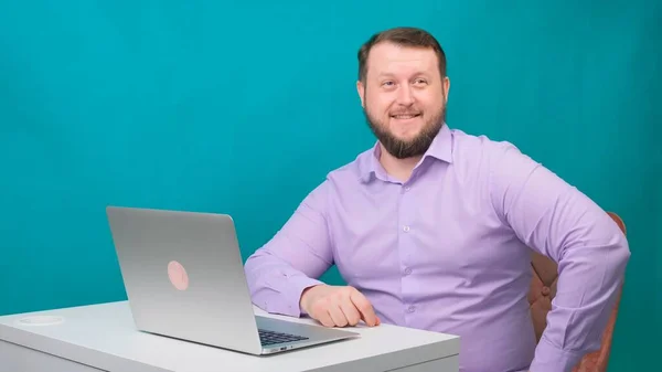 Jovem empresário feliz sorrindo e falando para a câmera. Retrato de um homem rindo enquanto olha para seu laptop. Homem trabalhando em sua mesa no escritório — Fotografia de Stock