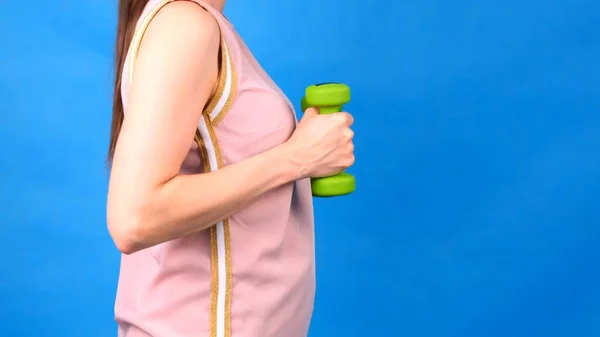 Λίπος Γυναίκα σε ένα ροζ αθλητικό κοστούμι με αλτήρες στα χέρια κάνει ασκήσεις σε μπλε φόντο. Η έννοια του αθλητισμού, διατροφή και απώλεια βάρους. — Φωτογραφία Αρχείου