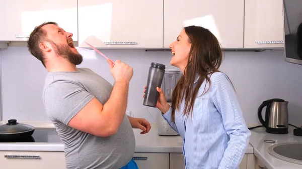 Привлекательные молодые радостные пара мужчина и женщина весело танцуют и поют во время приготовления пищи на кухне дома. — стоковое фото