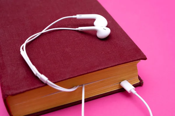 Livro de áudio com fones de ouvido isolados em fundo rosa — Fotografia de Stock