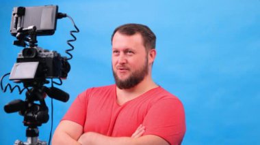 Pembe tişörtlü genç şişman adam mavi arka planda video bloğu yapıyor..
