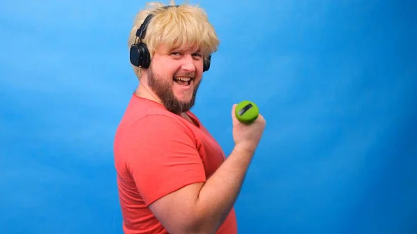 Hombre gordo divertido con mancuernas haciendo ejercicios sobre un fondo azul. —  Fotos de Stock