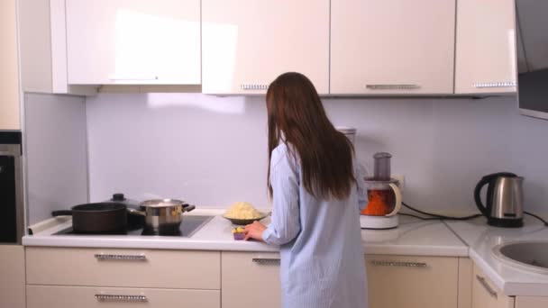 Молодая и красивая домохозяйка готовит на белой кухне. — стоковое видео