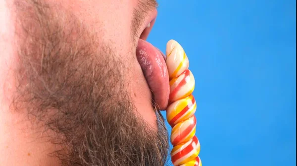 Чоловік сексуально лиже цукерки льодяник на синьому фоні . — стокове фото