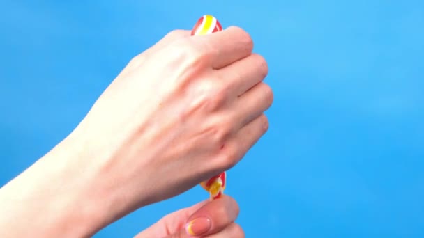 Close up of female hands. In a female hand a candy lollipop, on the other hand, a woman imitates masturbation. Blue simple background. — Stock Video