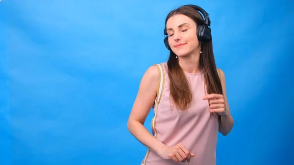 Hermosa chica de energía con auriculares escuchando música sobre un fondo azul en el estudio — Foto de Stock