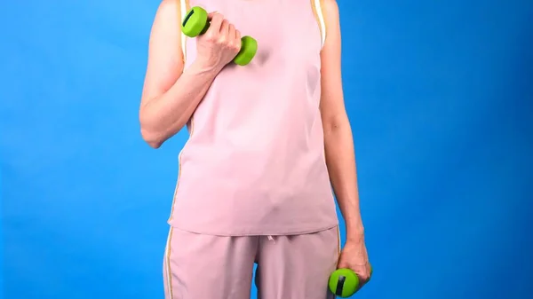 Dicke Frau im rosafarbenen Sportanzug mit Hanteln in den Händen macht Übungen auf blauem Hintergrund. Das Konzept von Sport, Ernährung und Gewichtsverlust. — Stockfoto