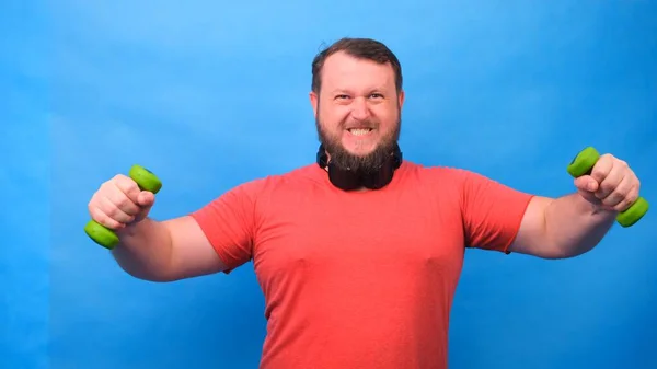 Elegante hombre en una camiseta rosa con mancuernas divertido hacer ejercicios sobre un fondo azul —  Fotos de Stock