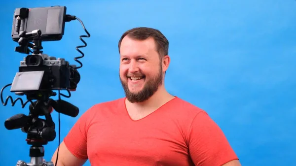 Joven gordo en una camiseta rosa hace un video blog sobre un fondo azul . —  Fotos de Stock