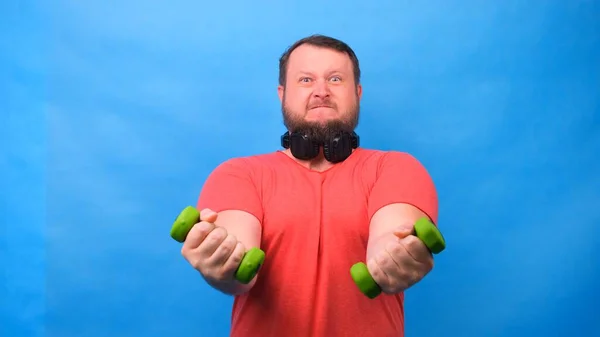 핑크 티셔츠를 입고 파란 배경에 이상 한 운동을 하는 뚱뚱 한 남자. — 스톡 사진