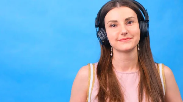 Retrato de una alegre alumna feliz escuchando música con auriculares y bailando aislada sobre un fondo azul —  Fotos de Stock