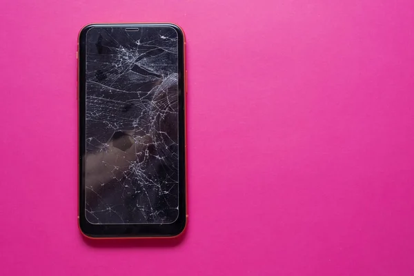 Broken glass mobile phone screen on a pink background.