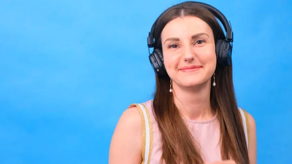 Енергетична дівчина з навушниками, що слухають музику на синьому фоні в студії, крупним планом — стокове фото