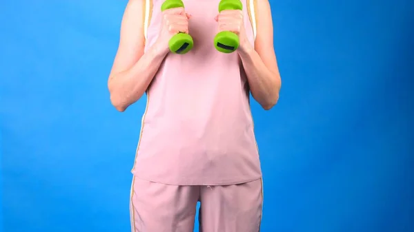 Eine Frau im rosafarbenen Sportanzug mit Hanteln in den Händen macht Übungen auf blauem Hintergrund. Das Konzept von Sport, Ernährung und Gewichtsverlust. — Stockfoto