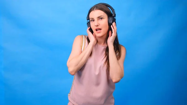 Beautiful Energy Girl with headphones listening to music on a blue background in the studio — Stock Photo, Image