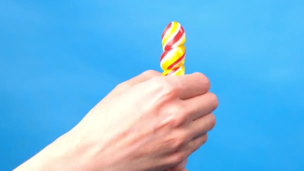 Close up of female hands. In a female hand a candy lollipop, on the other hand, a woman imitates masturbation. Blue simple background. — Stock Video
