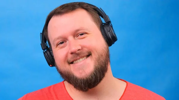 一个快乐迷人的胖男人，戴着耳机，穿着蓝色背景的粉色T恤。听音乐，唱歌跳舞 — 图库照片