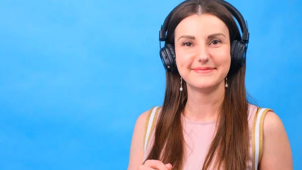 Retrato de uma menina alegre e feliz estudante com ouvir música com fones de ouvido e dançar isolado sobre um fundo azul — Fotografia de Stock