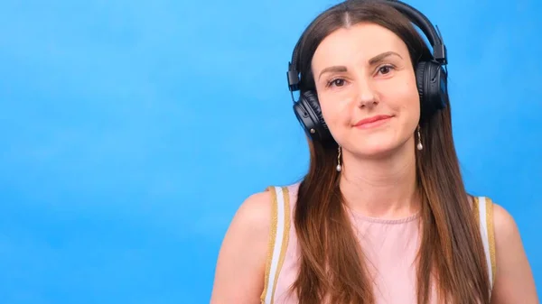 Energia ragazza con le cuffie ascoltare musica su uno sfondo blu in studio, primo piano — Foto Stock