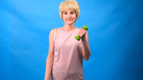 Lustige Frau in Perücke mit weißem Haar und grünen Hanteln in den Händen, die Übungen auf blauem Hintergrund machen — Stockfoto