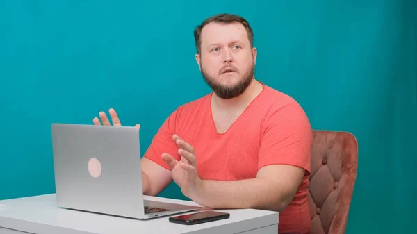 Joven hombre de negocios feliz en una camiseta rosa trabaja en un ordenador portátil y habla con la cámara en una pantalla verde. Retrato de un hombre hablando mirando en su portátil. Hombre trabajando en su escritorio en la oficina . — Foto de Stock