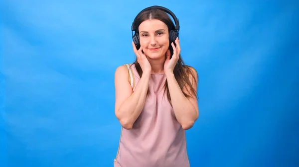 Portrait of a cheerful happy girl student with listening to music with headphones and dancing isolated over a blue background — Stock Photo, Image