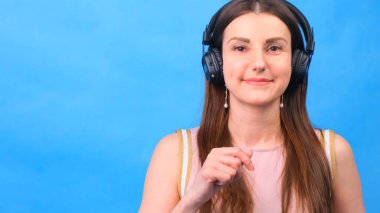 Kulaklıklı enerji kızı stüdyoda mavi bir arkaplanda müzik dinliyor.