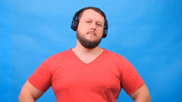 Vrolijke charismatische dikke man in hoofdtelefoon geïsoleerd en roze t-shirt op een blauwe achtergrond. luisteren naar muziek, zingen en dansen — Stockfoto