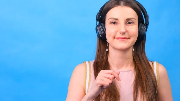 Energy girl with headphones listening to music on a blue background in the studio, closeup — Stock Photo, Image