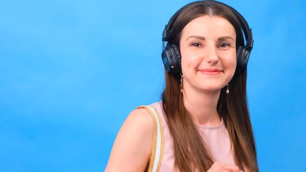 Energy girl with headphones listening to music on a blue background in the studio, closeup — Stock Photo, Image