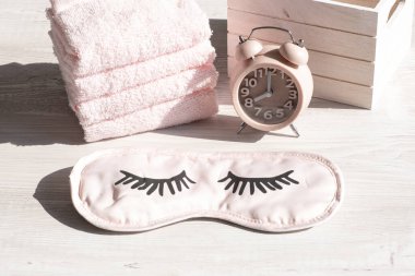 Çalar saat ve uyku maskesi, sabahları ya da gün batımında tahta beyaz bir masada havlu. Sabah ve akşam hijyen prosedürleri, kişisel bakım. Boşluğu kopyala