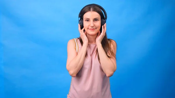 Beautiful Energy Girl with headphones listening to music on a blue background in the studio — Stock Photo, Image