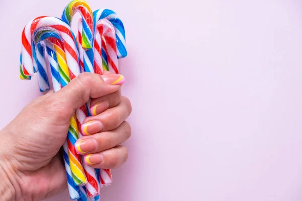 Mano femminile tiene un sacco di bastoncini di caramelle multicolore su uno sfondo rosa, spazio copia — Foto Stock