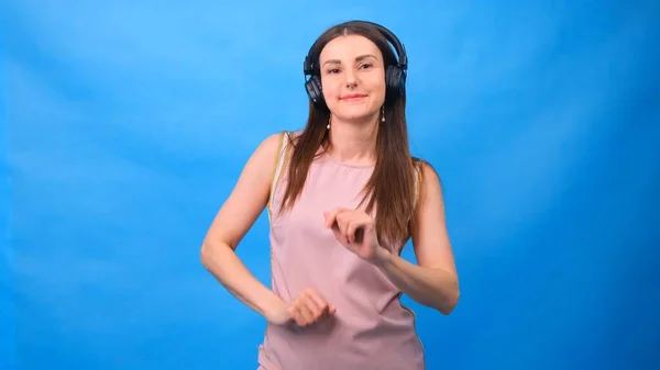 Brunette vrouw in luistert naar muziek met hoofdtelefoon op een blauwe achtergrond. — Stockfoto