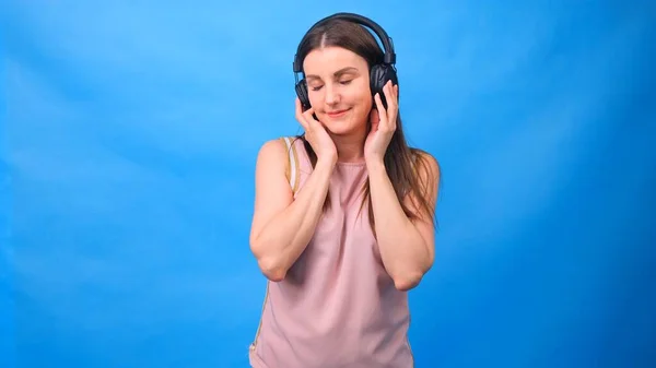 Brunette female in listens to music with headphones on a blue background. — Stock Photo, Image