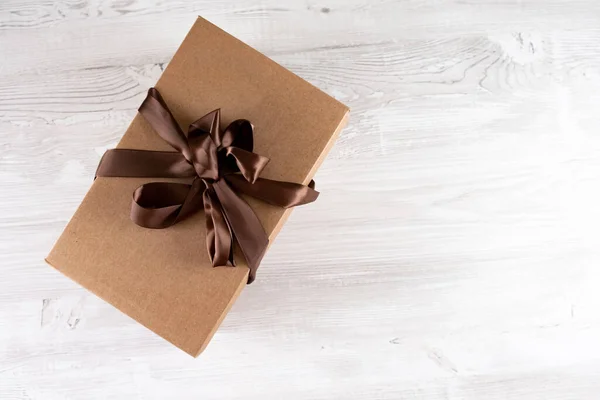 Pudełko kartonowe z brązowym łukiem na białym drewnianym stole, koncepcja usługi dostawy — Zdjęcie stockowe