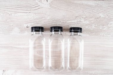 Üç plastik şeffaf boş şişe ve ahşap bir masanın üzerinde siyah bir kapak. Logon için bir yer var. Boşluğu kopyala