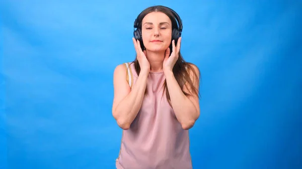 Brunette female in listens to music with headphones on a blue background. — Stock Photo, Image