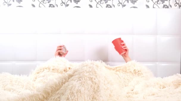 Attraktiv ung kvinna går upp i sängen med en kopp kaffe och en väckarklocka. Kvinnan försov sig och är sen, reagerar med fasa på den tiden. — Stockvideo