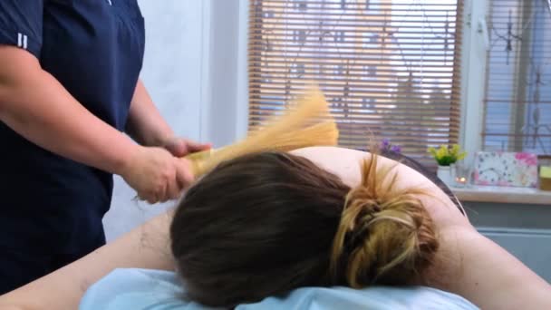 Massageterapeut gör en anti-celluliter massage till en fet kvinna på ett massagebord i ett spa med en bambupinne. Spabehandlingar. Hälsa och skönhet, kost — Stockvideo