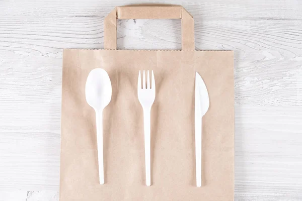 Catering and street fast food plastic fork, spoon, knife on paper bag.Eco-friendly food packaging and cotton eco bags on gray background with copy space. Carering of nature and recycling concept. — Stock Image Catering and street fast food plastic fork, spoon, knife on paper bag.Eco-friendly food packaging and cotton eco bags on gray background with copy space. Carering of nature and recycling concept. Stock Photo