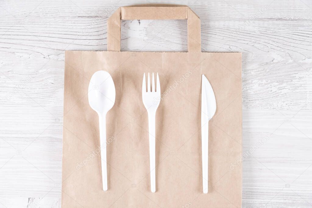 Catering and street fast food plastic fork, spoon, knife on paper bag.Eco-friendly food packaging and cotton eco bags on gray background with copy space. Carering of nature and recycling concept.