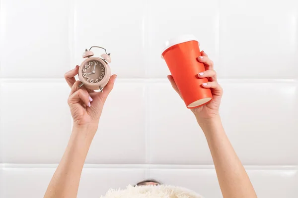 Mãos femininas com uma xícara de café e um despertador na cama, o conceito de começar um novo dia, bom dia. Iniciar um novo negócio. — Fotografia de Stock