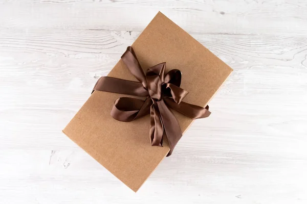 Pudełko na białym drewnianym tle. Koncepcja dostarczania paczek, dostawa do kwarantanny od koronawirusa. Pudełko tekturowe z kokardą. — Zdjęcie stockowe