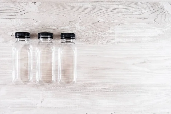 Três garrafas transparentes de plástico com uma tampa preta em uma mesa de madeira. Há um lugar para o seu logotipo. Espaço de cópia. — Fotografia de Stock